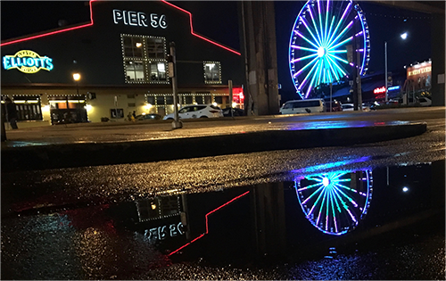 Example of Night Photograph. Wonderwheel and Pier 56 building at night with reflection in puddle in downtown Seattle.